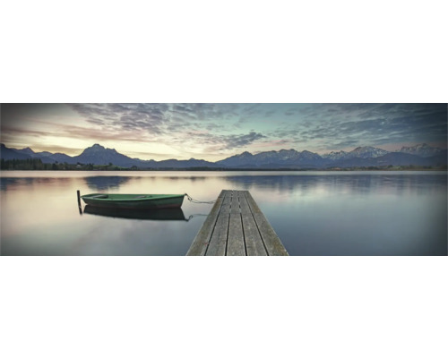 THE WALL Decopaneel Ochtendhumeur landschap meer 155x53 cm Een rustig meer met een houten steiger en een kleine boot op de voorgrond, met een berglandschap op de achtergrond.