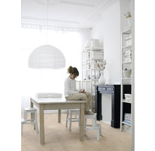 Lichte kamer met houten vloer, grote tafel, papieren lamp en een kind dat op een kruk zit