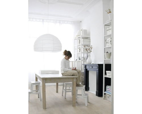 Lichte ruimte met tafel, stoelen, boekenkasten en een meisje dat op een kruk zit