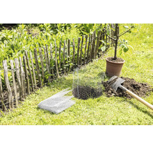 Tuinscene met lattenhek, spade, gaas en boom in pot