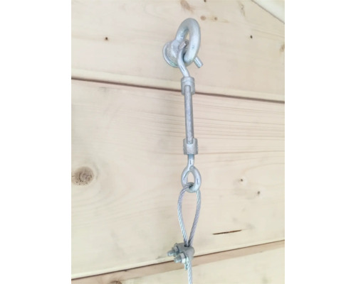 Detailopname van een staalkabel met spanschroef en ringmoer aan een houten wand.