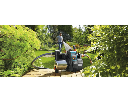 Hydrofoorpomp in gebruik voor tuinbesproeiing met een man op de achtergrond die een gazonsproeier bedient.