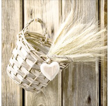 Decoratieve wilgenmand met houten hart en graanaren voor een houten muur