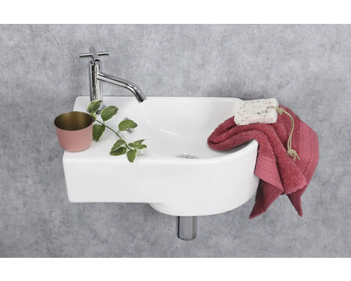 Kleine wastafel met kraan, plant, zeep en handdoek voor een grijze muur