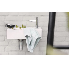 Wastafel met kraan, handdoek en accessoires tegen een bakstenen muur