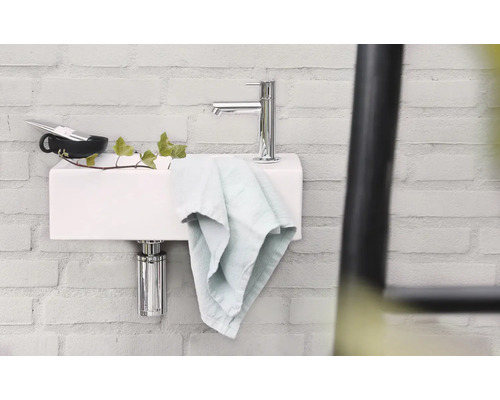 Wastafel met kraan, handdoek en accessoires tegen een bakstenen muur