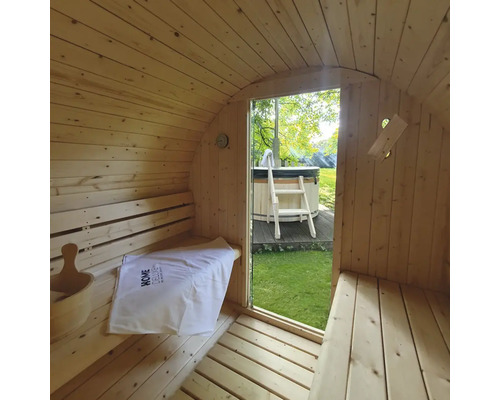 Interieur van een houten barrel sauna met uitzicht op een bubbelbad in de tuin.