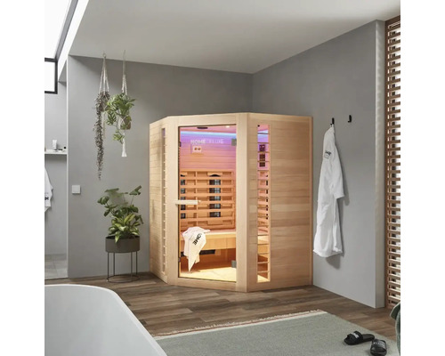 Houten infraroodsauna in een badkamer met bad, handdoeken en planten.