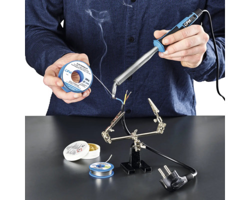 Persoon soldeert kabels met soldeerbout, soldeertin en soldeerpasta op een werkvlak.