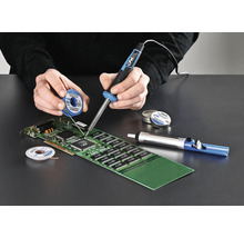 Persoon soldeert een printplaat met een soldeerbout, soldeertin en desoldeerpomp.