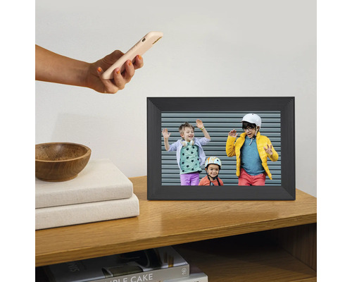 Digitale fotolijst op een houten plank met een foto van drie kinderen en een hand die een smartphone vasthoudt