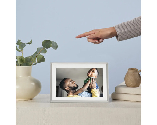 Digitale fotolijst met foto van een vader en zijn zoon op een tafel, naast een vaas met eucalyptus en een hand die naar de lijst wijst.