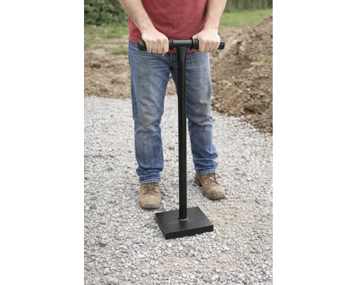 Een man gebruikt een handstamper om de grond te verdichten.