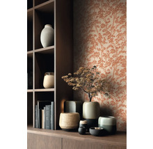 Vliesbehang met dennenpatroon in roestlook achter een donkerhouten kast met keramieken vazen en boeken.