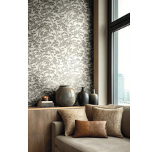 Vliesbehang met dennenboompatroon in een woonkamer met bank, sierkussens en keramische vazen op een dressoir naast een raam.