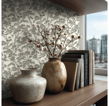Vliesbehang met boompatroon in schetsstijl op een muur achter een houten plank met keramieken vazen en boeken in een lichte kamer.