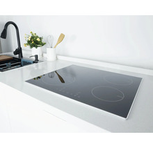 Inductiekookplaat met vier kookzones in een lichte, moderne keuken op een wit aanrechtblad naast de gootsteen en kraan.