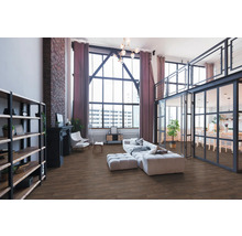 Ruime loft-woonkamer in industriële stijl met vloer in houtlook, grote raampartijen, bakstenen muur en moderne meubels.