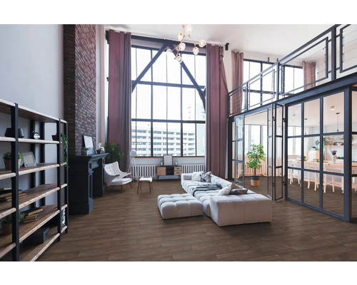 Ruime loft-woonkamer in industriële stijl met vloer in houtlook, grote raampartijen, bakstenen muur en moderne meubels.