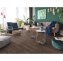 Woonkamer met donkere vloer in houtlook, grijze bank, blauwe fauteuil en groene muur met kamerplanten. Modern en licht ingericht.