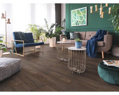 Woonkamer met donkere vloer in houtlook, grijze bank, blauwe fauteuil en groene muur met kamerplanten. Modern en licht ingericht.
