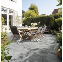 Modern terras met grijze vloertegels in steenlook, een houten tafel en klapstoelen in een lichte, verzorgde tuin.