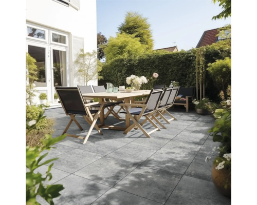 Modern terras met grijze vloertegels in steenlook, een houten tafel en klapstoelen in een lichte, verzorgde tuin.