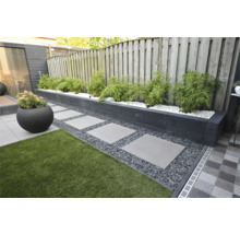 Moderne tuin met verhoogde border van donkere stapelblokken, bamboe in wit grind, stapelstenen in donker split en kunstgras.