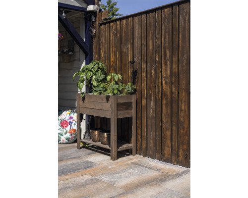 Een houten kweektafel met groene planten op een terras voor een donkere houten schutting.