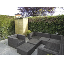 Tuinlounge set van grijs polyrotan en een houten tuinkast voor een groene heg op een stenen terras.