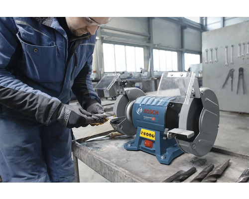 Bosch Professional dubbele slijpmachine in een werkplaats, een vakman slijpt een gereedschap met rondvliegende vonken.