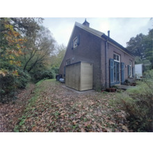 Houten tuinkast tegen de muur van een bakstenen huis in een herfstige tuin met bladeren.