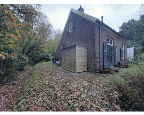 Houten tuinkast tegen de muur van een bakstenen huis in een herfstige tuin met bladeren.