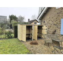 Open houten tuinkast met planken in een tuin naast een stenen huis.