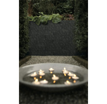 Donkere muurstenen in een modern ingerichte tuin met grindpad, hagen en een schaal met brandende drijfkaarsen.