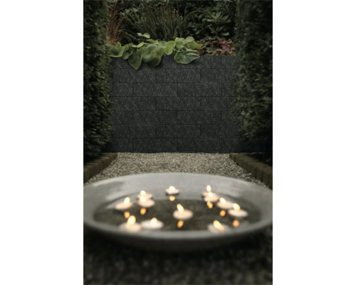 Donkere muurstenen in een modern ingerichte tuin met grindpad, hagen en een schaal met brandende drijfkaarsen.
