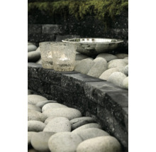 Modern tuinontwerp met zwarte stapelblokken, grijze rivierkeien, glazen windlichten en een decoratieve mozaïekschaal.