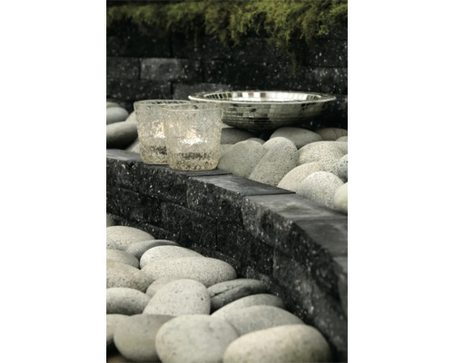 Modern tuinontwerp met zwarte stapelblokken, grijze rivierkeien, glazen windlichten en een decoratieve mozaïekschaal.