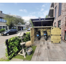 Open houten motorberging met twee motorfietsen op een betegelde ondergrond. Georganiseerde buitenscène met vogelhuisje en haag naast een gebouw.