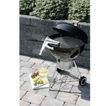 Zwarte houtskoolbarbecue met open deksel op een stenen terras, met roestvrijstalen rooster, asopvangbak en wielen.