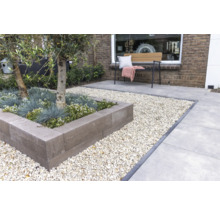Modern ingerichte tuin met een verhoogde border van grijze stapelblokken, omringd door licht grind en grote terrastegels.