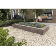 Moderne tuin met rechthoekige plantenbak van grijze stapelblokken, beplant met bomen en grassen, omgeven door licht grind.