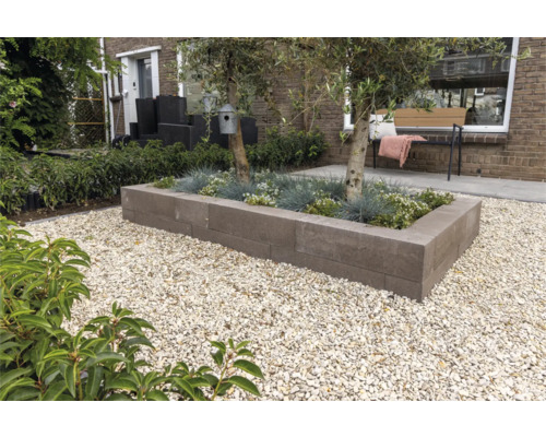 Moderne tuin met rechthoekige plantenbak van grijze stapelblokken, beplant met bomen en grassen, omgeven door licht grind.