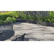 Modern, licht terras met zeshoekige terrastegels van beton, een donkere tuinmuur en tuinmeubilair in een tuin.