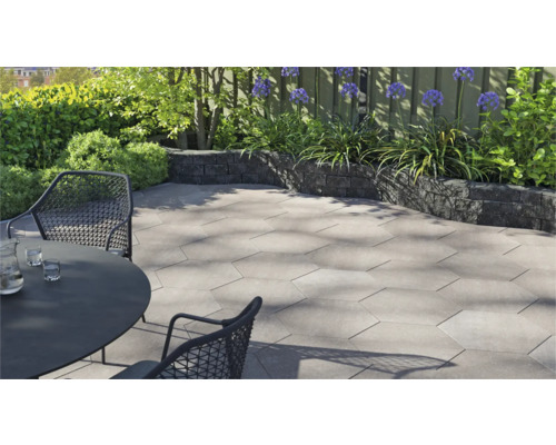 Modern, licht terras met zeshoekige terrastegels van beton, een donkere tuinmuur en tuinmeubilair in een tuin.