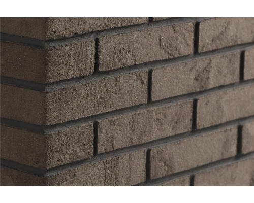 Steenstrips met baksteenlook met ruwe gestructureerde oppervlakte en donkere voegen op een muurhoek.