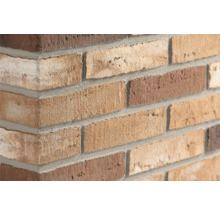 Close-up van een gemetselde hoek met steenstrips in diverse bruintinten en grijze voegen.