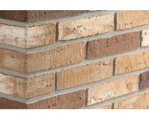 Close-up van een gemetselde hoek met steenstrips in diverse bruintinten en grijze voegen.
