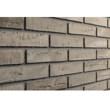 Grijsbruine steenstrips met een gestructureerd oppervlak, verwerkt als een bakstenen muur met donkere voegen.