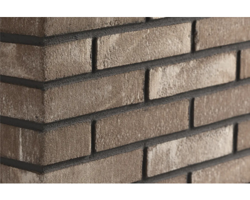 Grijsbruine steenstrips in baksteenlook met een gestructureerd oppervlak op een muurhoek.